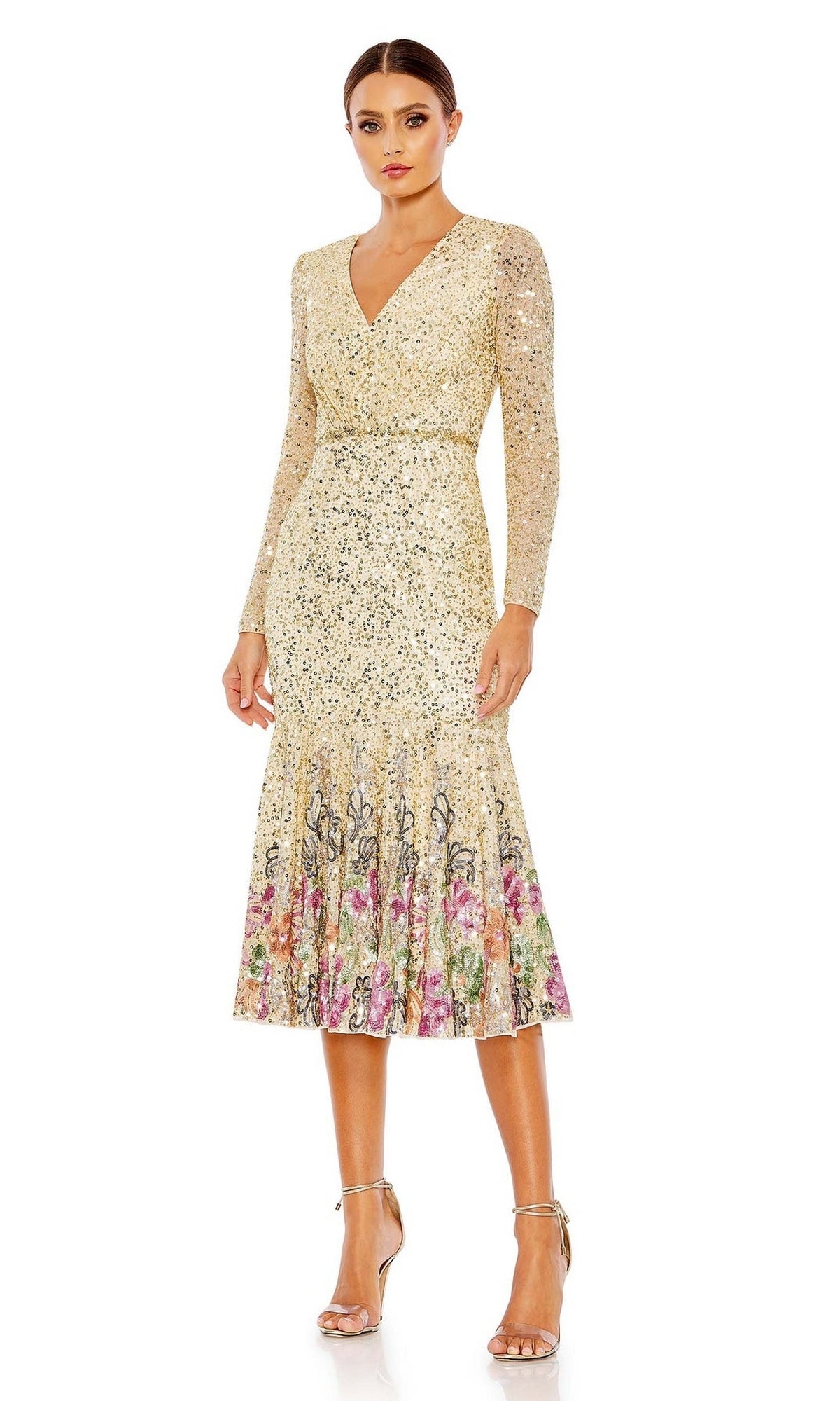A woman stands against a white background in the Mac Duggal 5589 Beaded Midi Wedding Guest Dress, featuring long sleeves, a V-neckline, floral hem details, and paired with silver high-heeled sandals.